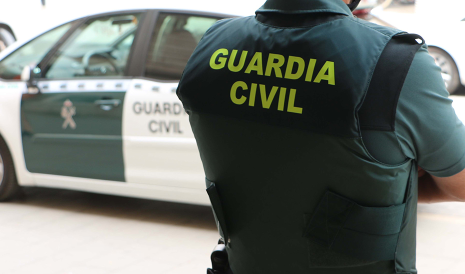 Agente de Guardia Civil junto a un coche oficial.